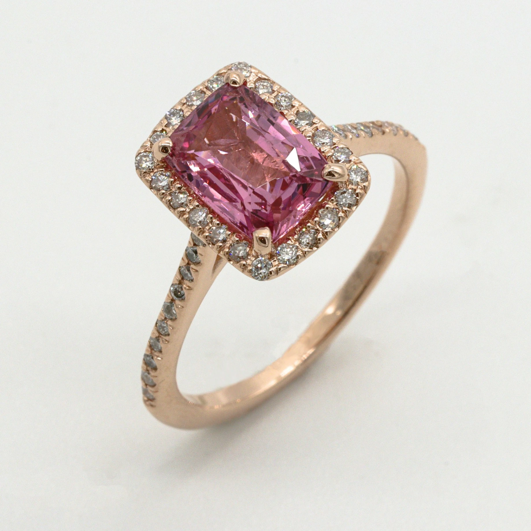 A rose gold ring with a rectangular pink gemstone surrounded by small diamonds